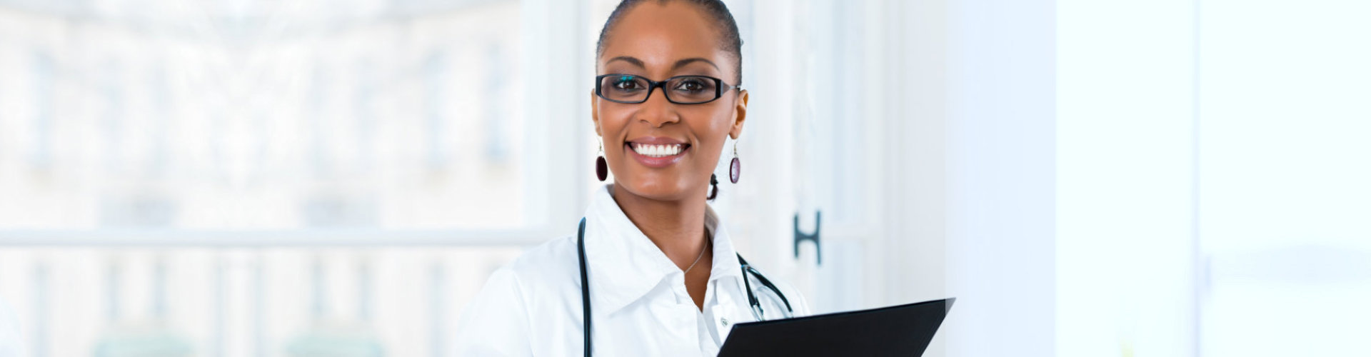 female doctor standing at a window in clinic wearing eyeglasses smiling