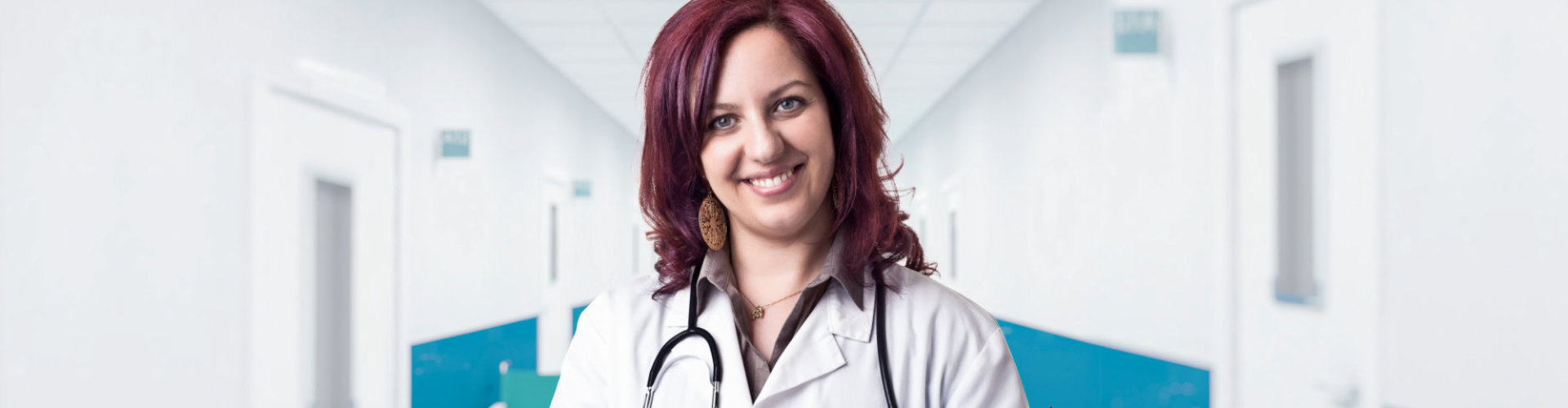 female doctor standing at a window in clinic wearing stethoscope smiling